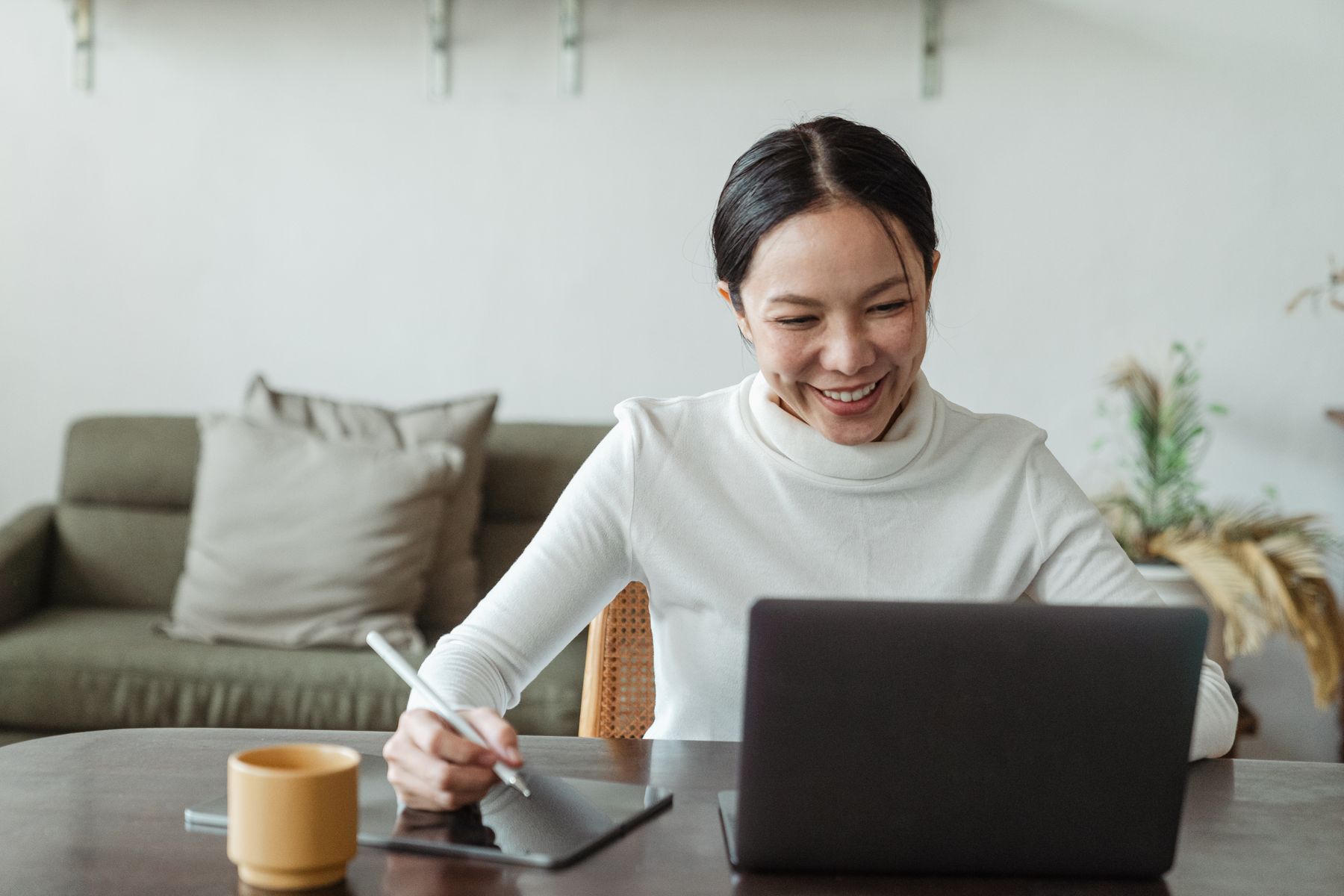 Woman smiling while using a laptop and writing notes