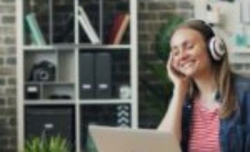 A woman wearing headphones while working at her laptop in a warm home office, illustrating intentional audio stimulation for ADHD focus