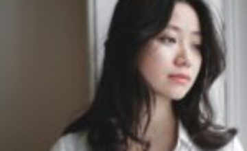 Reflective Asian adult by a window representing the hidden effort of autistic masking