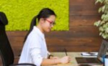 Asian woman writing notes at a desk in a modern office
