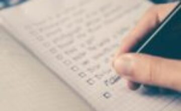A hand holding a pen over a clean daily planner beside a laptop and a warm cup of coffee.