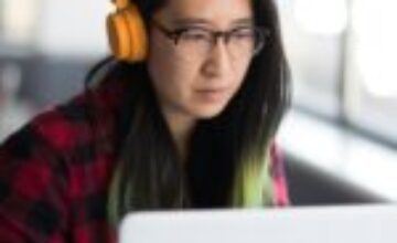 Woman wearing yellow headphones while working on a laptop